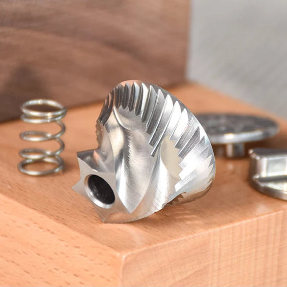 Full stainless steel conical burr on a wooden surface with text highlighting its features.